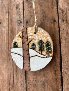 a wooden ornament hanging from a string on a wood surface with trees painted on it