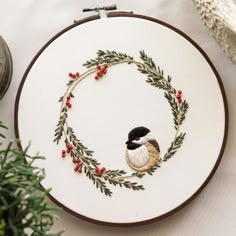 a cross stitch pattern with a bird in a circle surrounded by berries and greenery