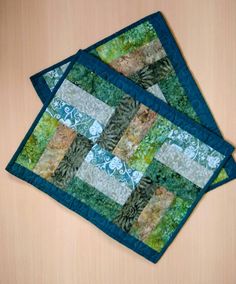 two quilted placemats sitting on top of a wooden table next to each other