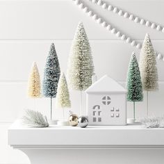 christmas trees and decorations on a mantle in front of a white wall