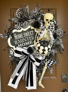 a halloween wreath with black and white decorations on the front door, featuring a skeleton holding a sign that says home sweet