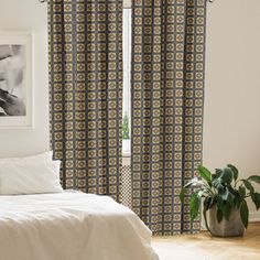 a white bed sitting next to a window with curtains on top of it and a plant in the corner