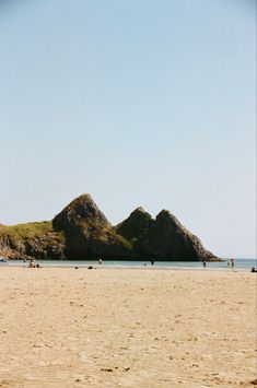 people are walking on the beach near some mountains