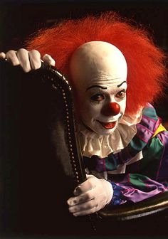 a creepy clown sitting in a chair with his arm around the back of it's head