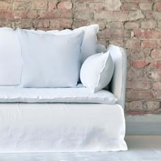 a white couch with pillows on it in front of a brick wall