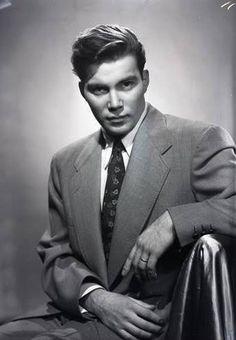 an old photo of a man in a suit and tie sitting on a chair with his legs crossed