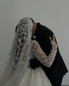 a bride and groom kissing in front of a white wall wearing wedding gowns with long sleeves