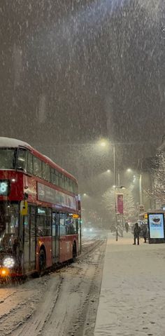 a red double decker bus driving down a snow covered street