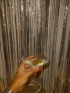 a person holding a wine glass in front of a wall with silver strips on it