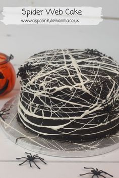 a spider web cake with white icing on a plate next to a jack - o'- lantern