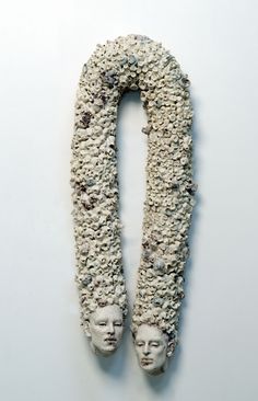 a sculpture made out of rocks and pebbles with two heads on each side, in front of a white wall