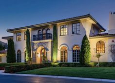 a large white house with lots of windows and plants on the front lawn at night