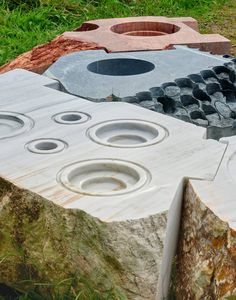 an outdoor fire pit made out of rock and cement with circles in the center, surrounded by green grass