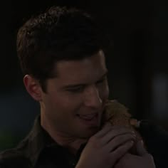 a young man is eating a sandwich in the dark with his hand on his chest