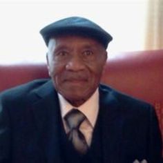 an older man in a suit and tie sitting on a red couch wearing a hat