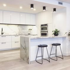 two stools are in front of the kitchen island with marble countertops and white cabinets