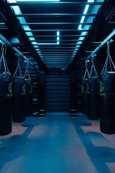 an empty gym with black boxing bags hanging from the ceiling and blue lighting on the ceiling