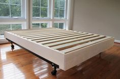 a bed frame sitting on top of a hard wood floor in front of two windows