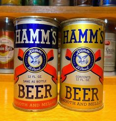 two cans of beer sitting on top of a wooden table next to each other in front of shelves