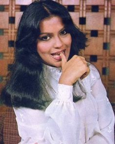 a woman with long black hair posing for a photo in front of a tiled wall