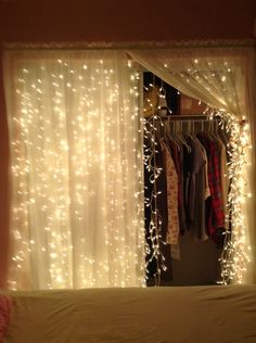 an open closet with clothes hanging on the rack and fairy lights strung across the curtain