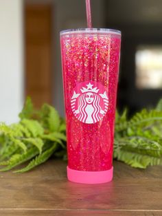 a pink starbucks cup sitting on top of a wooden table next to green leafy plants