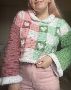 a woman with pink hair wearing a colorful sweater and smiling at the camera while holding her hands in her pockets