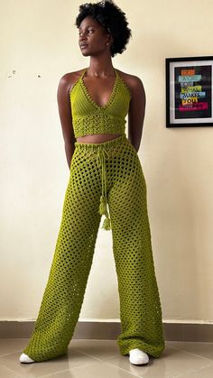 a woman standing in front of a wall wearing green crochet pants and crop top