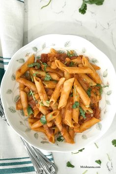 a white bowl filled with pasta and sauce on top of a green napkin next to silverware