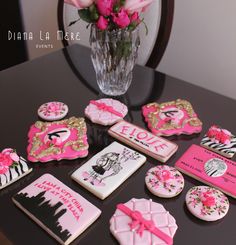 pink and black decorated cookies are sitting on a table next to a vase with roses