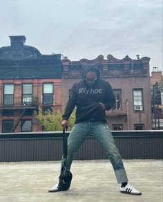 a man holding a guitar case while standing on top of a cement floor in front of buildings