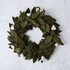 a green wreath with white pom - poms is on a marble countertop