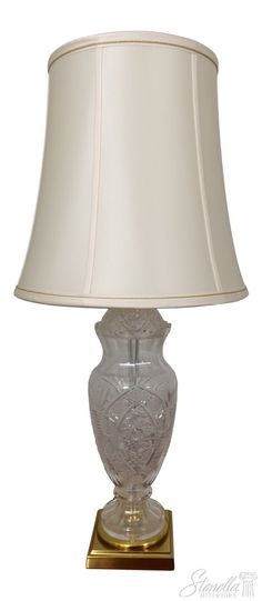 a glass lamp with a white shade on it's base and a gold base