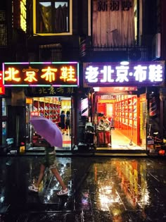 a person with an umbrella is walking down the street in front of a store at night