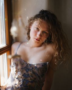 a young woman in a dress looking out the window at something outside she is holding