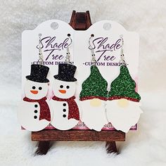 "Christmas Shaped faux leather earrings feature an adorable Snowman and Gnome! The Snowman has a black hat that can be glitter or solid and the scarf can be made in any color you wish, glitter or solid. The Gnome's hat can be customized to you color choice, also in glitter or solid.  Size: 2\" length x 1.1\" wide, with a 2.75\" drop (contact me if you want a different size) Shown is Snowman with black glitter hat and red glitter scarf, Gnome with green and red glitter hat." Glitter Scarf, Leather Christmas, Cricket Projects, Gnome Hat, Leather Ideas, Faux Leather Earrings, The Snowman, Cute Snowman, Christmas Earrings