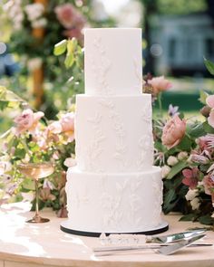 a three tiered white wedding cake sitting on top of a table next to flowers