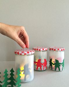 someone is decorating three small jars with christmas decorations on the inside and one holding a lit candle