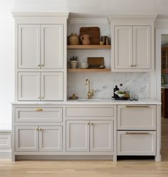 a kitchen with white cabinets and marble counter tops, gold pulls on the cupboards