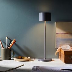 a desk with a lamp, pencils and other office supplies on it in front of a blue wall