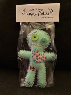 a green stuffed animal in a package on a black surface with a white sign behind it