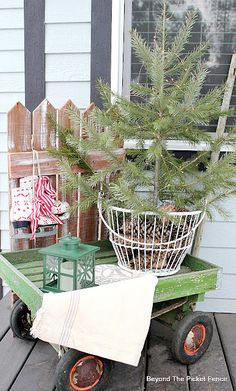 a green wagon with a christmas tree in it on a porch next to a fence