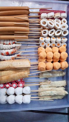 several skewers of food are arranged in a plastic container with chopsticks and marshmallows