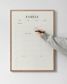 a person writing on a family calendar in front of a white wall with a wooden frame