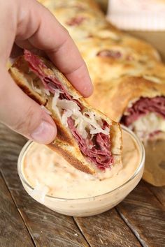 a person holding a sandwich in their hand and dipping it into a small bowl on the table