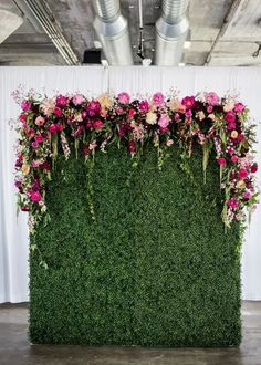 an artificial green wall with pink flowers and greenery on the top, in front of a white backdrop