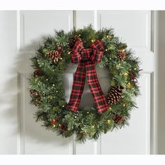 a christmas wreath hanging on the front door with pine cones and red plaid ribbon tied around it