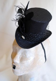 This simple and elegant gothic mini top hat is covered with beautiful black silk shantung. It is embellished with black veil, a luxurious spray of curled ostrich plums and a sparkling flower shaped rhinestone button. Also available in white and ivory here : https://www.etsy.com/shop/BizarreNoir?ref=seller-platform-mcnav&section_id=14329940 If you're interested in another color, please, send me a message to talk about your options. This mini top hat is fully lined with satin and attaches to t Gothic Costume Hat With Round Crown For Costume Party, Black Gothic Mini Hats For Costume Party, Gothic High Crown Costume Accessories For Party, Gothic Top Hat With High Crown For Parties, Gothic Black Top Hat For Costume Party, Gothic Top Hat With Short Brim For Halloween, Black Gothic Top Hat For Costume Party, Steampunk Fitted Top Hat For Halloween, Black Gothic Mini Hat With Adjustable Fit