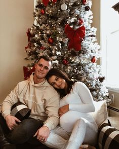 a man and woman sitting in front of a christmas tree