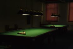 two green pool tables in a dimly lit room